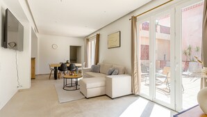 Un salon moderne avec un canapé d’angle, un coin repas comprenant une table et des chaises, et une porte-fenêtre coulissante donnant sur une terrasse extérieure.