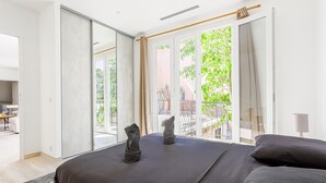 Une chambre moderne avec un grand lit, une porte-fenêtre coulissante donnant sur un balcon et un petit coin bureau.