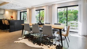 Un espace repas moderne avec une grande table, des chaises et une cuisine en arrière-plan.