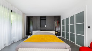 Une chambre moderne avec un grand lit, un dressing et une vue sur l’extérieur depuis la porte.