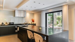 Une cuisine moderne dotée d’un îlot central, de meubles de rangement aux couleurs sombres et d’une grande fenêtre donnant sur un paysage verdoyant.