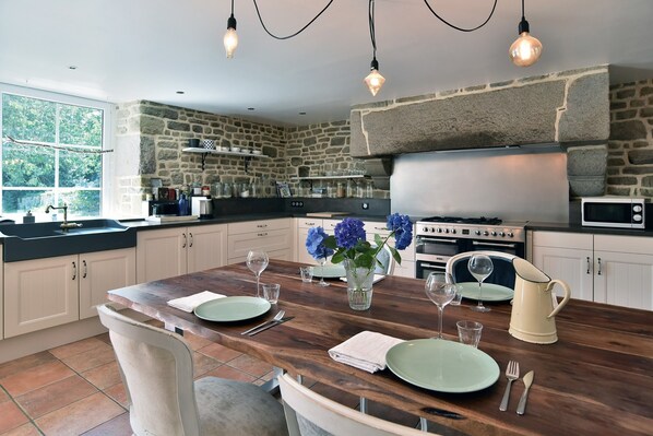 A kitchen with stone walls, a wooden dining table set with plates, glasses, and a vase of flowers. - La Bloutière - Avec grand jardin (La Bloutière)