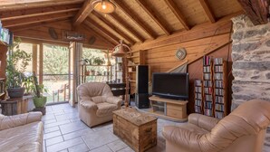 A cozy living room with wooden beams, a fireplace, leather sofas, a TV, and a bookshelf.