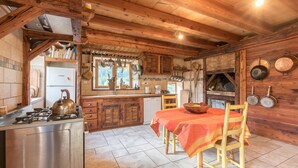 A rustic kitchen with wooden beams, a gas stove, a wooden table with chairs, and a brick oven.
