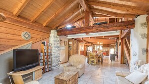 A spacious living room with a wooden ceiling, a television on a wooden stand, a stone pillar, and a stone wall.