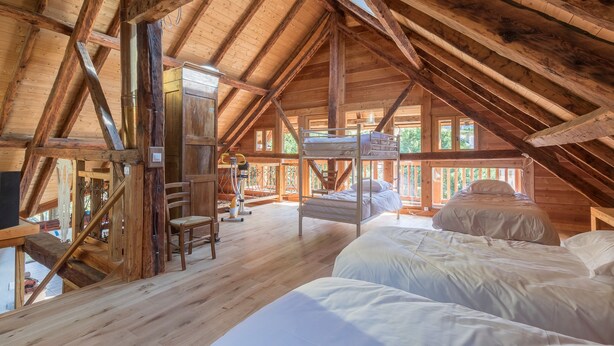 A rustic wooden cabin with a high ceiling, a bunk bed, a desk, and a chair.