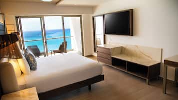 A modern hotel room with a large bed, a flat-screen TV, a desk, and a view of the ocean.