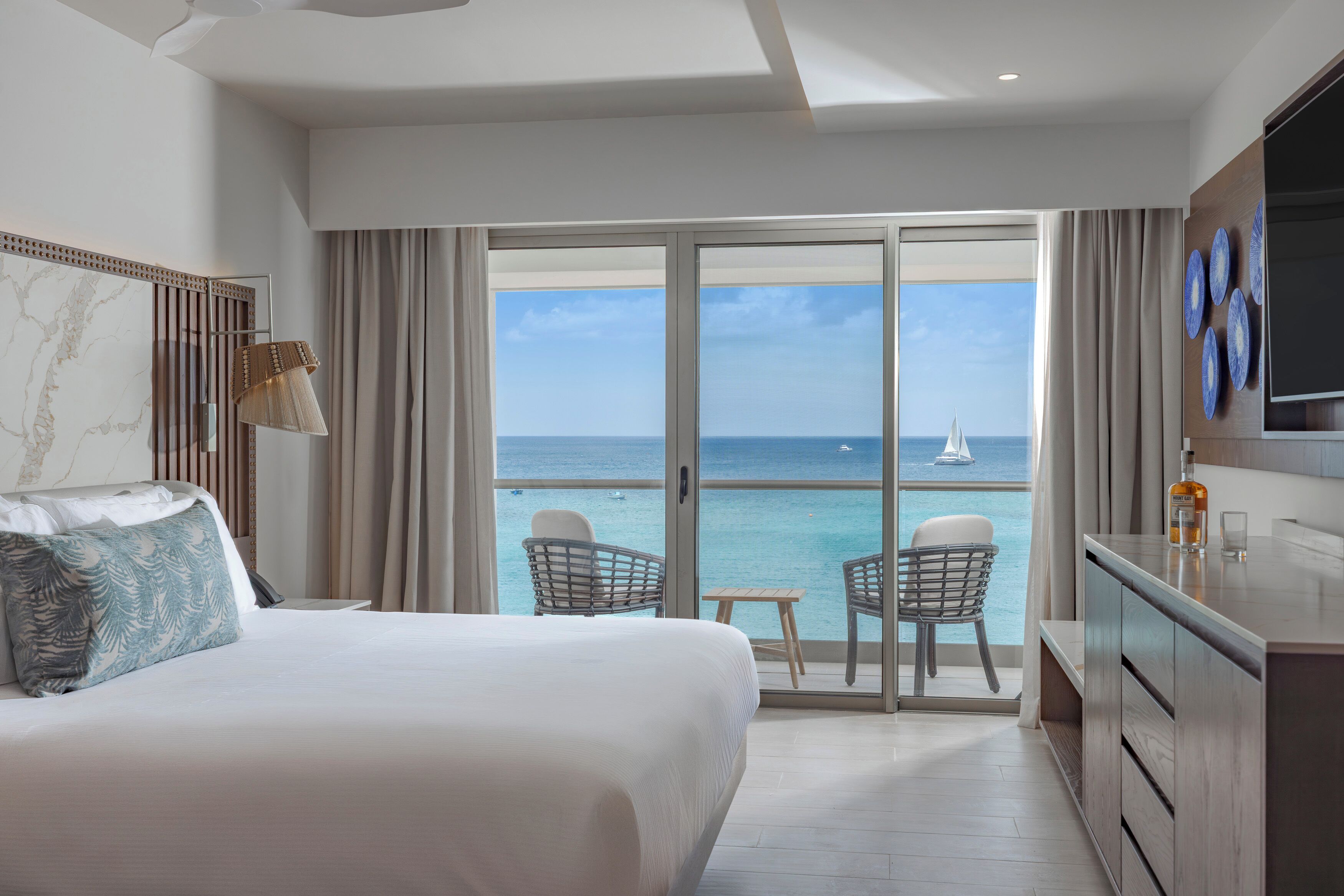 A hotel room with a bed, a television, a minibar, and a balcony with a view of the sea.