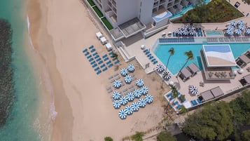 An aerial view of a resort with a beach, multiple pools, and sun umbrellas.