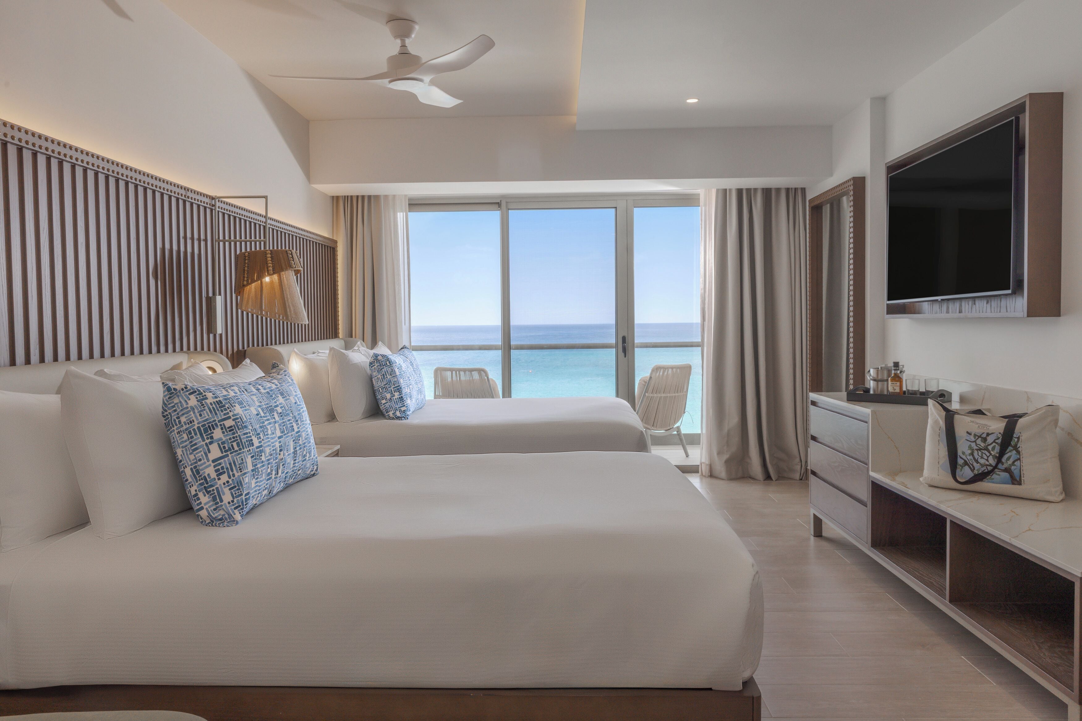 A hotel room with two beds, a TV, a desk, and a view of the ocean.