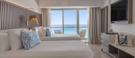 A hotel room with two beds, a TV, a desk, and a view of the ocean.