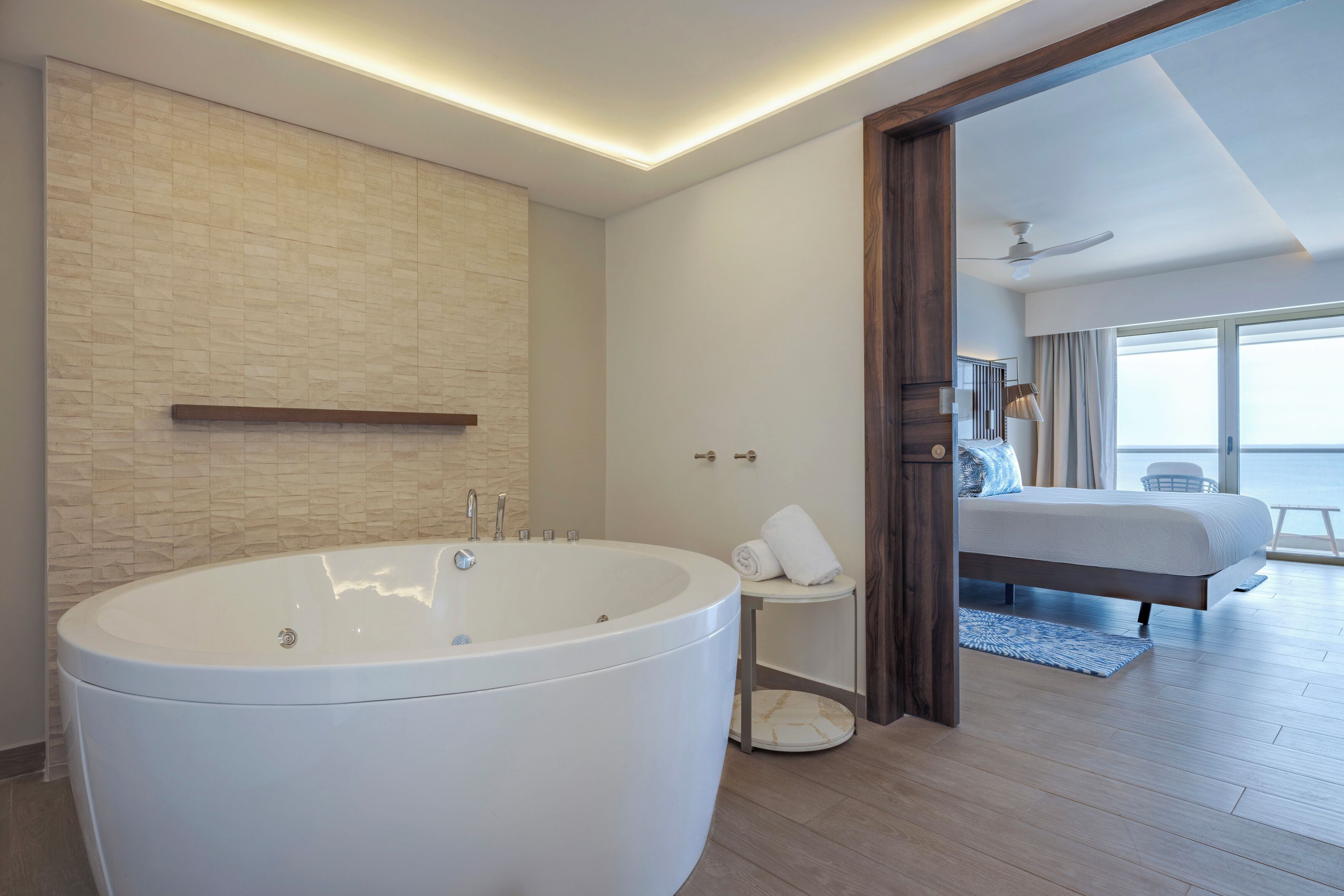 A modern bathroom with a freestanding bathtub, a small bedside table, and a towel.
