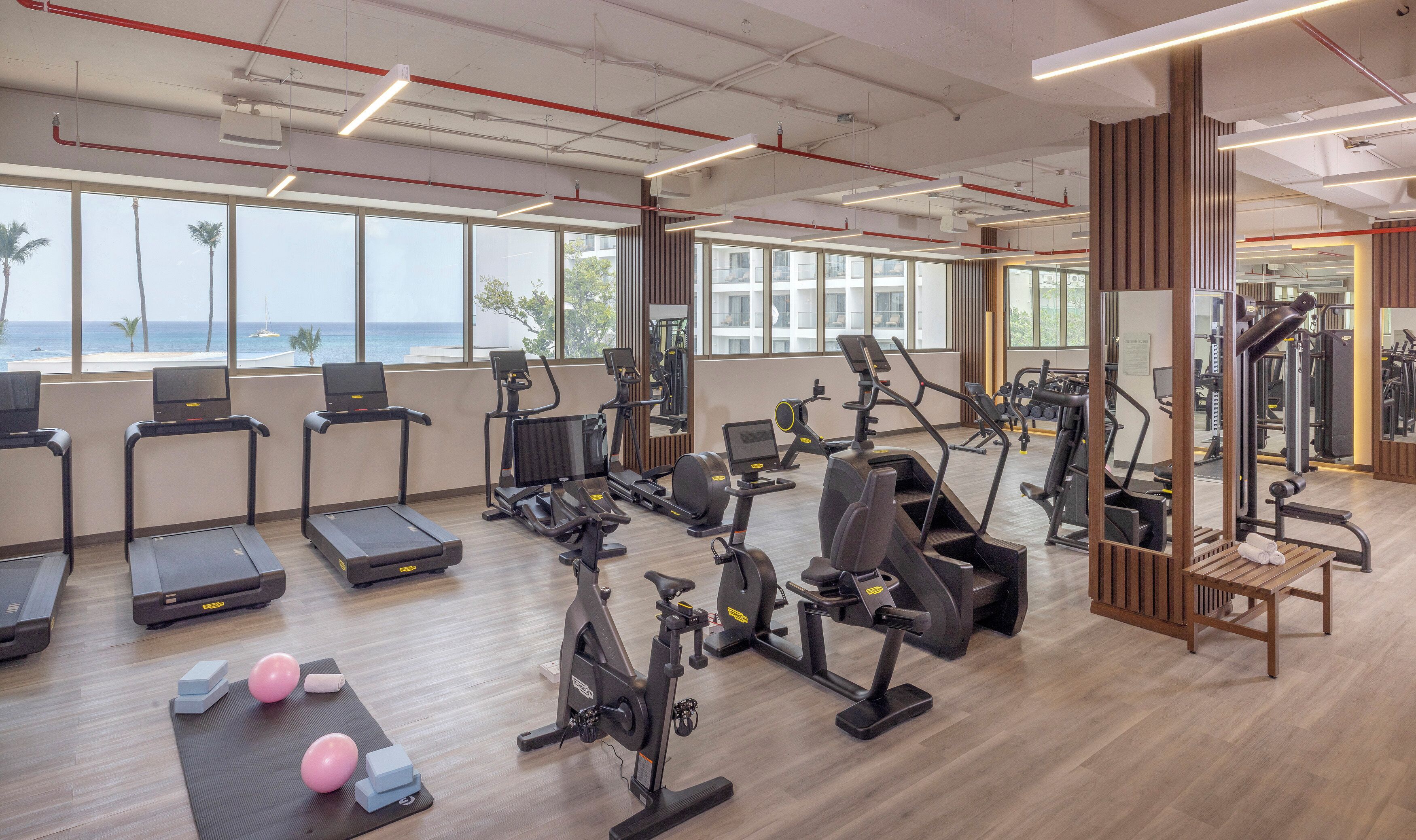 A gym with treadmills, stationary bikes, and exercise equipment, large windows, and a view of the ocean.