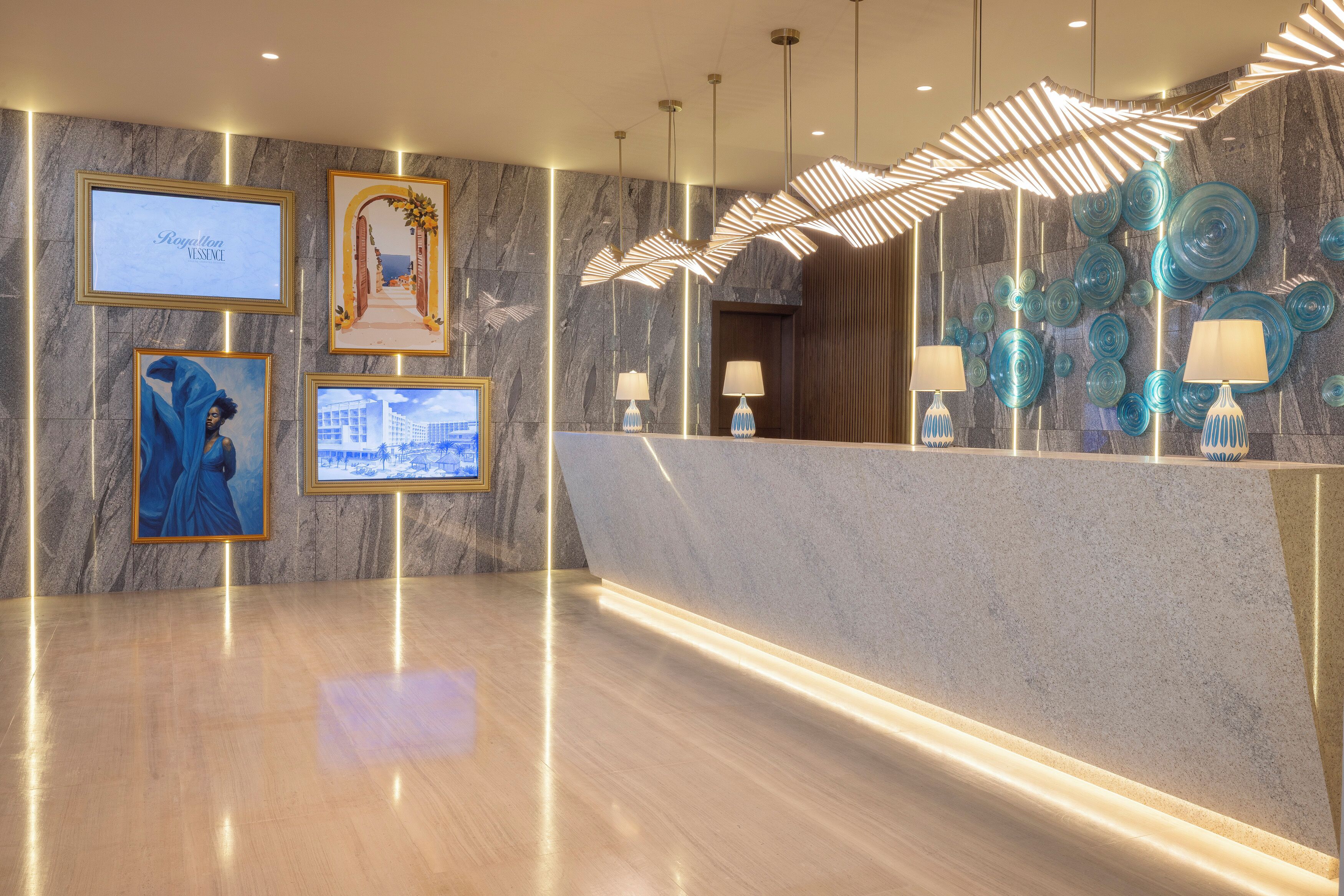 A modern hotel lobby with marble walls, framed artwork, and a reception desk with decorative lamps.