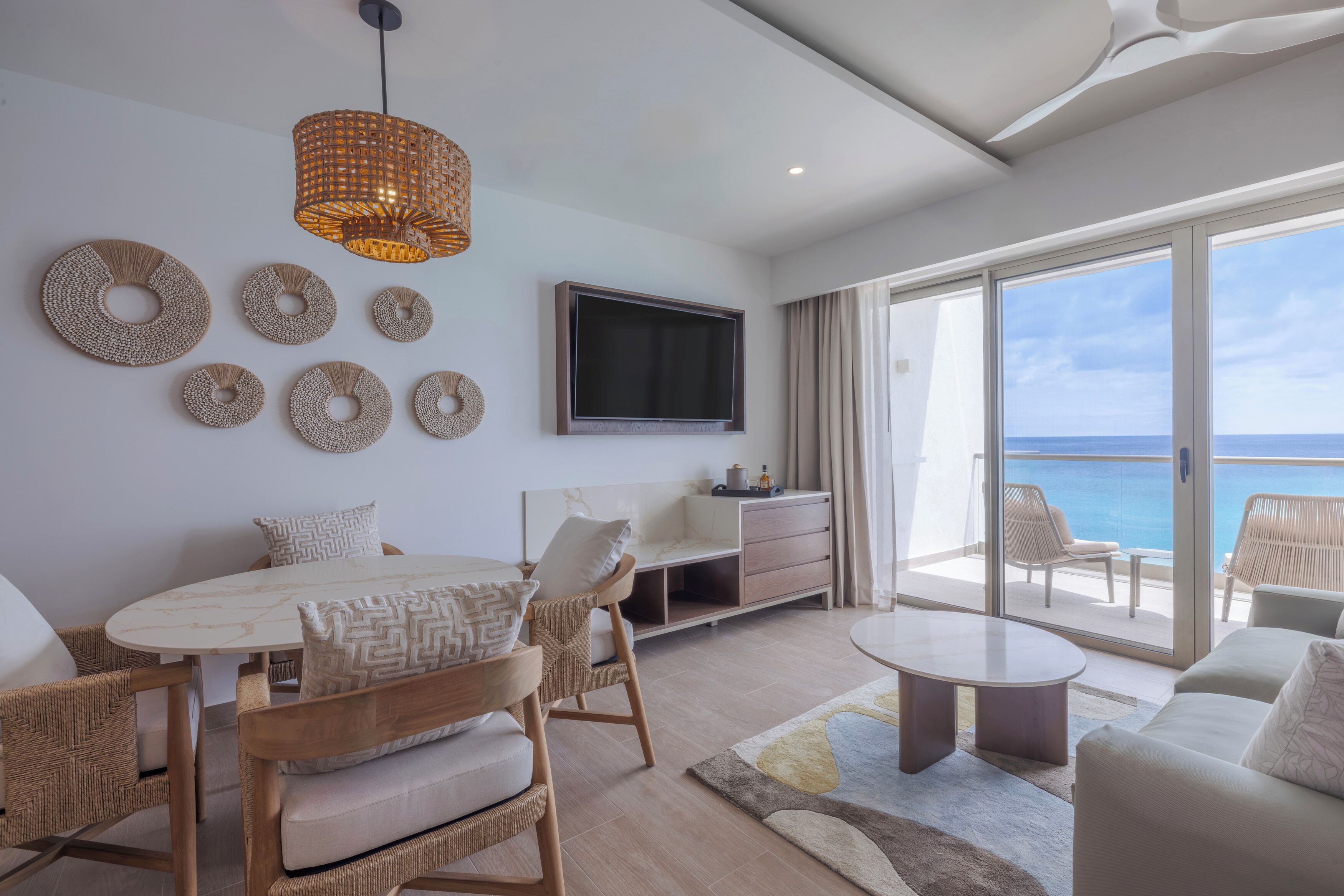 Una sala de estar moderna con comedor, un televisor de pantalla plana montado en la pared y un balcón con vista al mar.