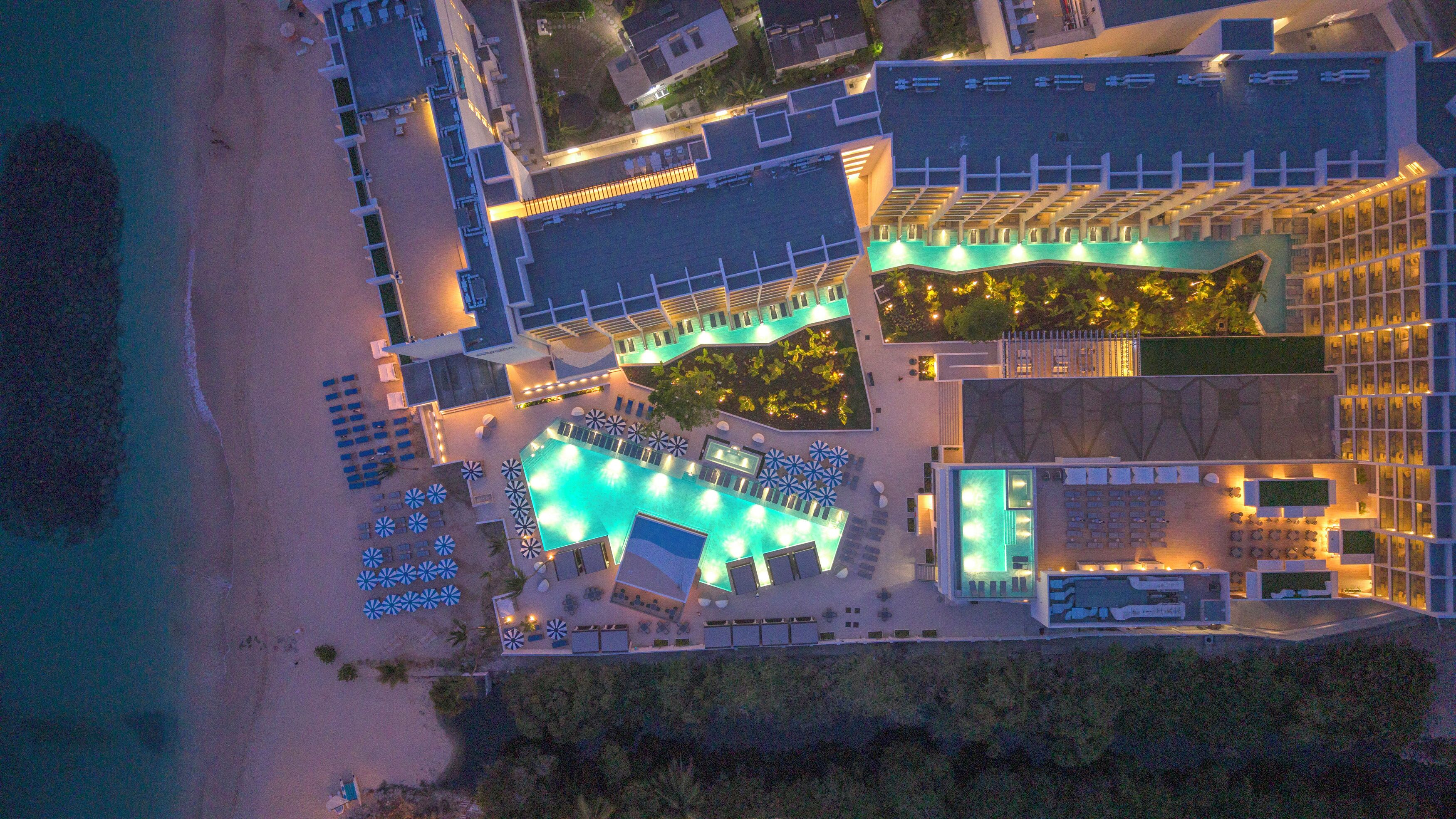 An aerial view of a resort with a swimming pool, sun loungers, and a beach area.