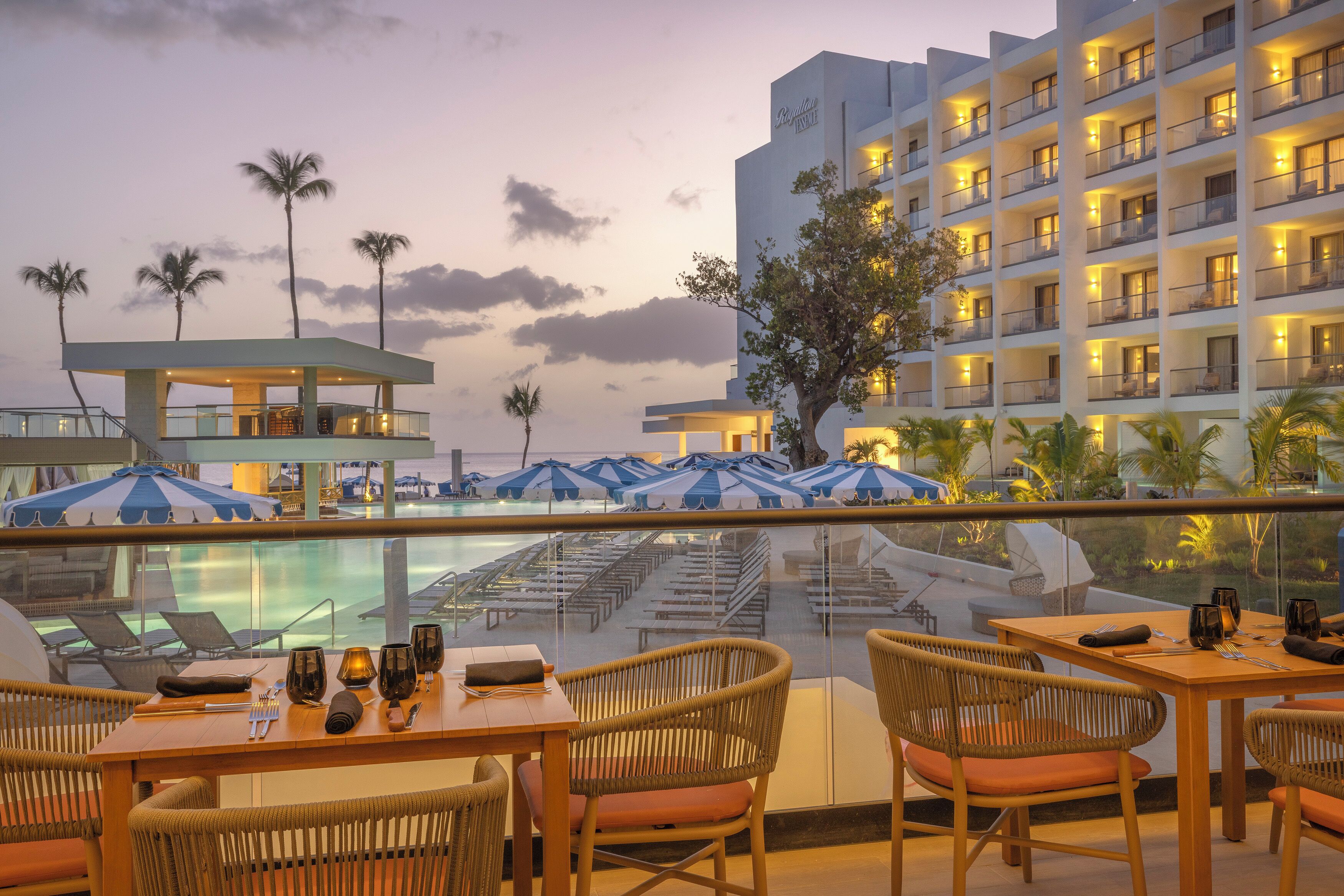 Un hotel con piscina, sillas de descanso y un comedor con mobiliario de mimbre.