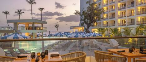 Un hotel con piscina, sillas de descanso y un comedor con mobiliario de mimbre.