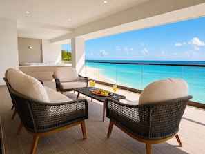 Varanda com mobiliário de vime, uma mesa com frutas e bebidas, e vista para o oceano.