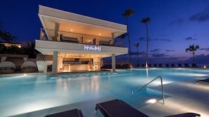 Un hotel moderno con piscina, sillones de descanso y una zona de bar.