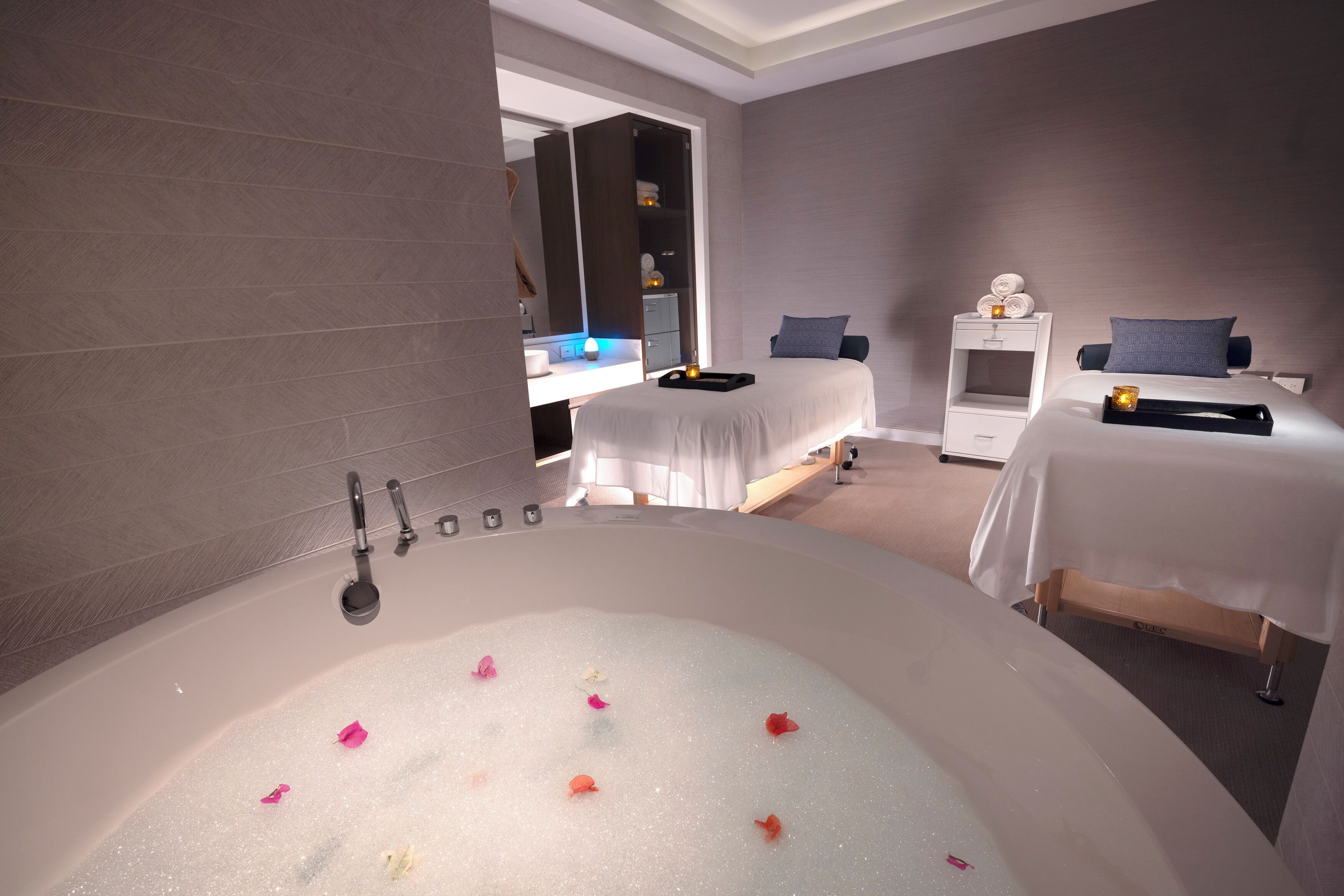 A hotel room with a large bathtub, two beds, a wardrobe, and a bedside table with a lamp.