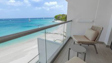 A balcony with a view of a beach and ocean, a chair, and a small table.