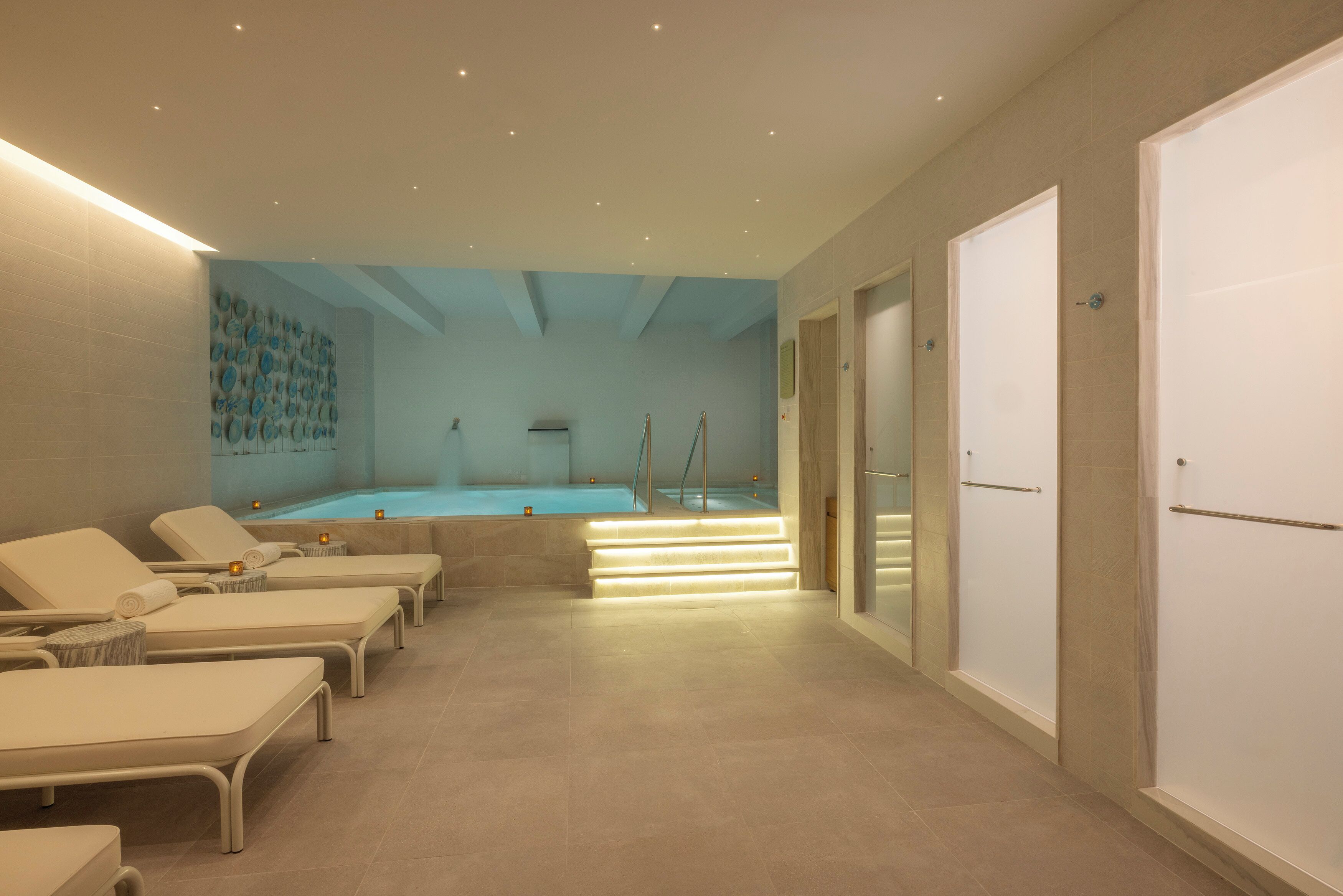 A spa area with lounge chairs, a pool, and a staircase leading to a changing room.