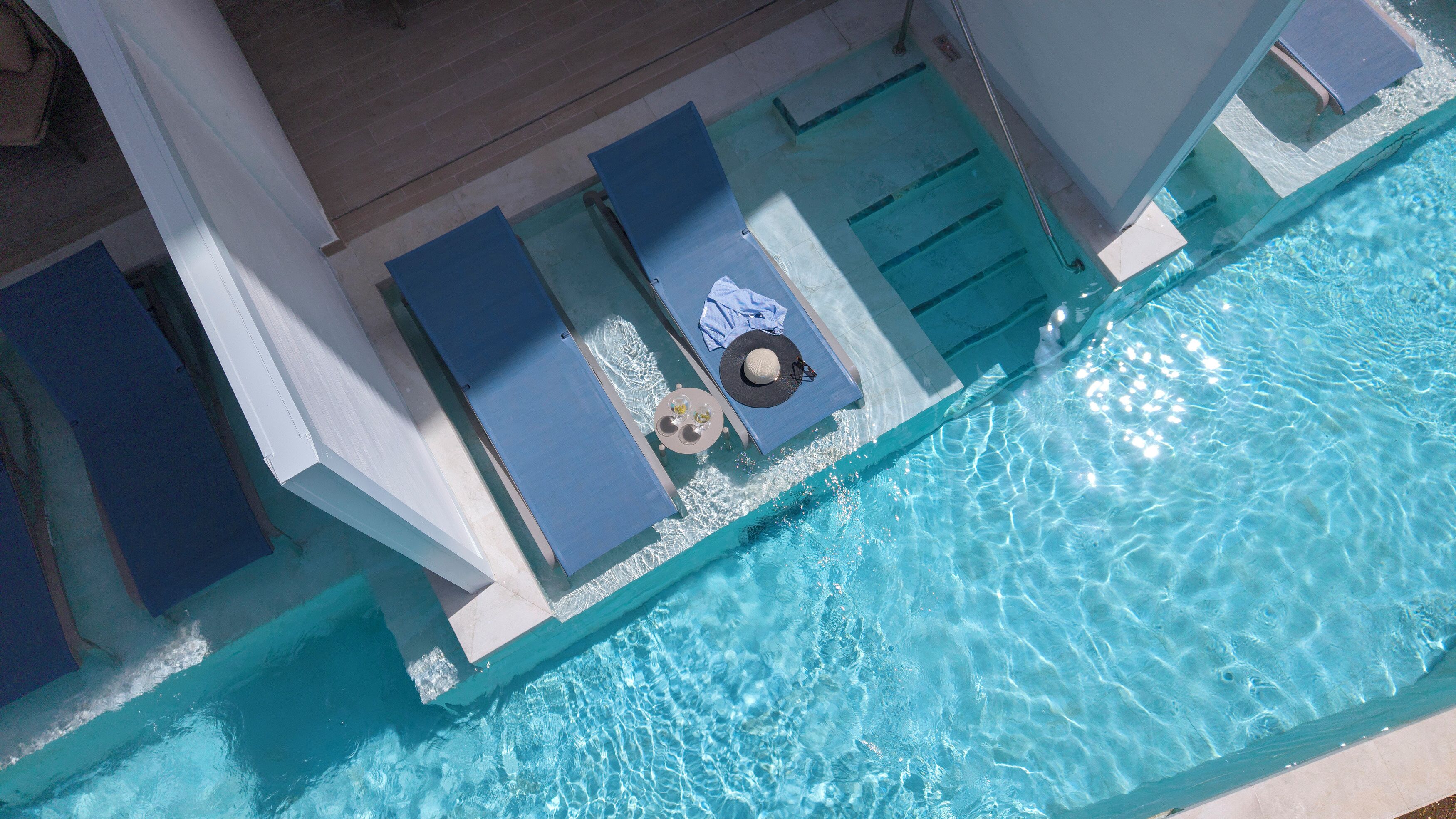 Vue aérienne d’une piscine avec des chaises longues et un transat.