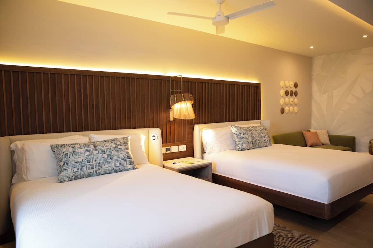 A hotel room with two beds, a ceiling fan, and a wall-mounted light fixture.