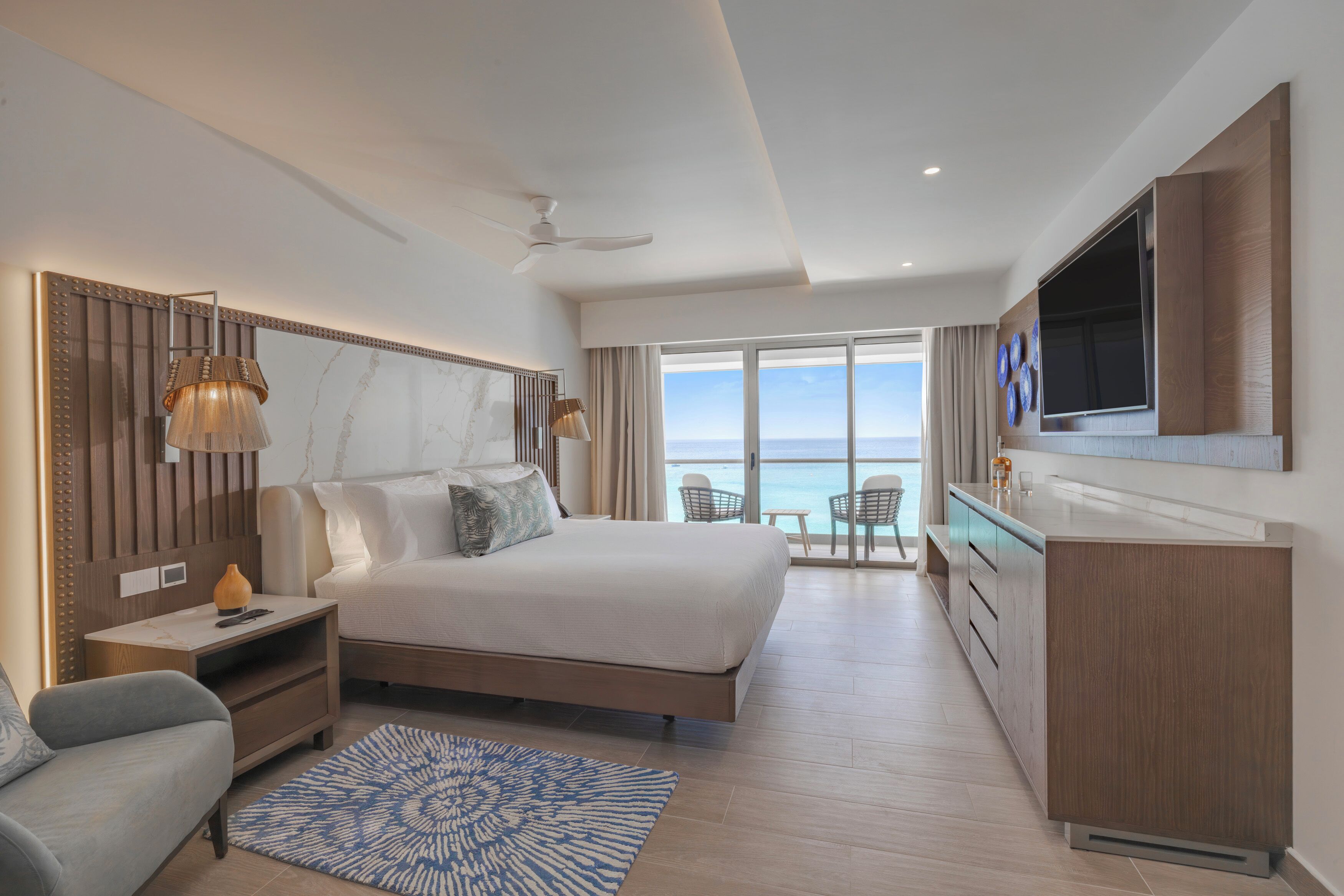 Une chambre d’hôtel moderne dotée d’un grand lit, d’un bureau, d’une télévision et d’un balcon offrant une vue sur la mer.