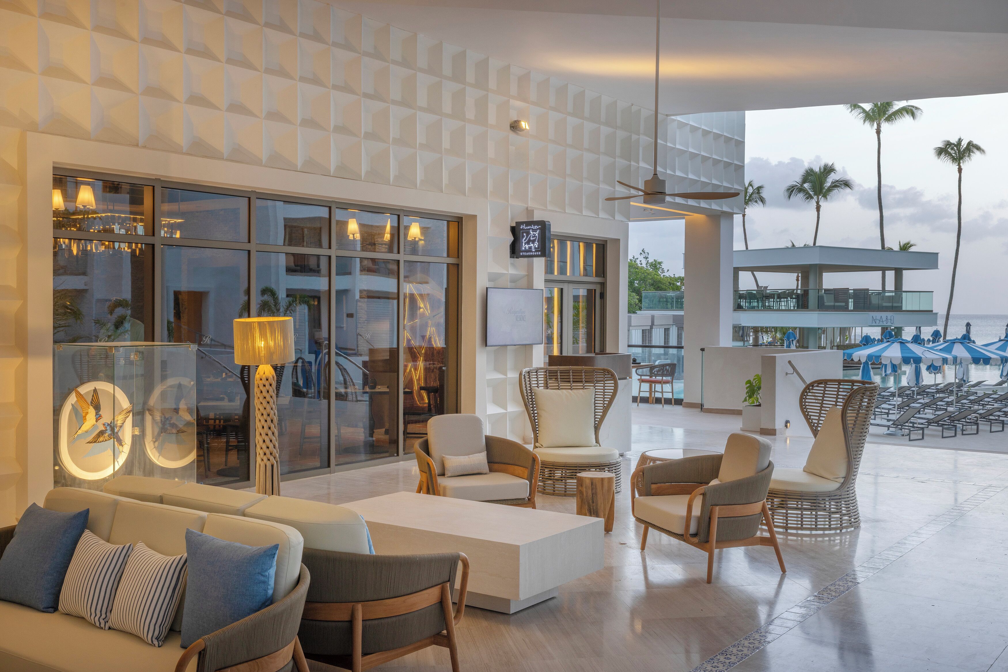 A modern lounge area with seating, a TV, and a view of the beach.