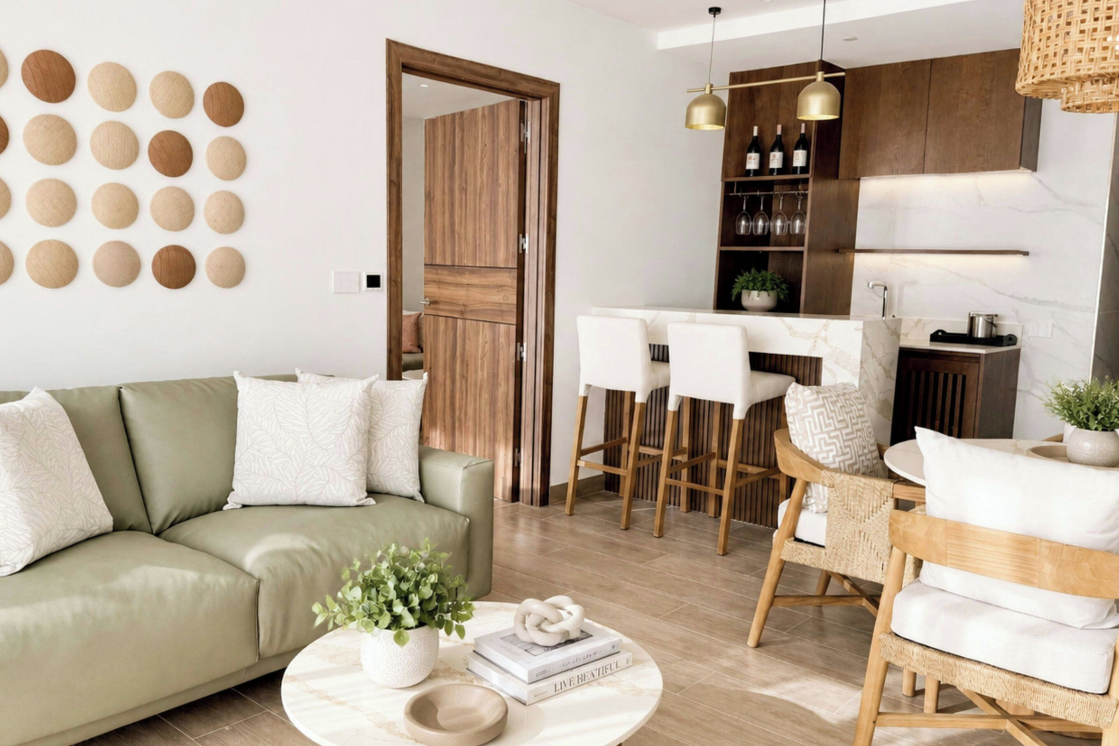 A modern living room with a green sofa, a round coffee table with books and a plant, and a dining area with white chairs and a wooden table.