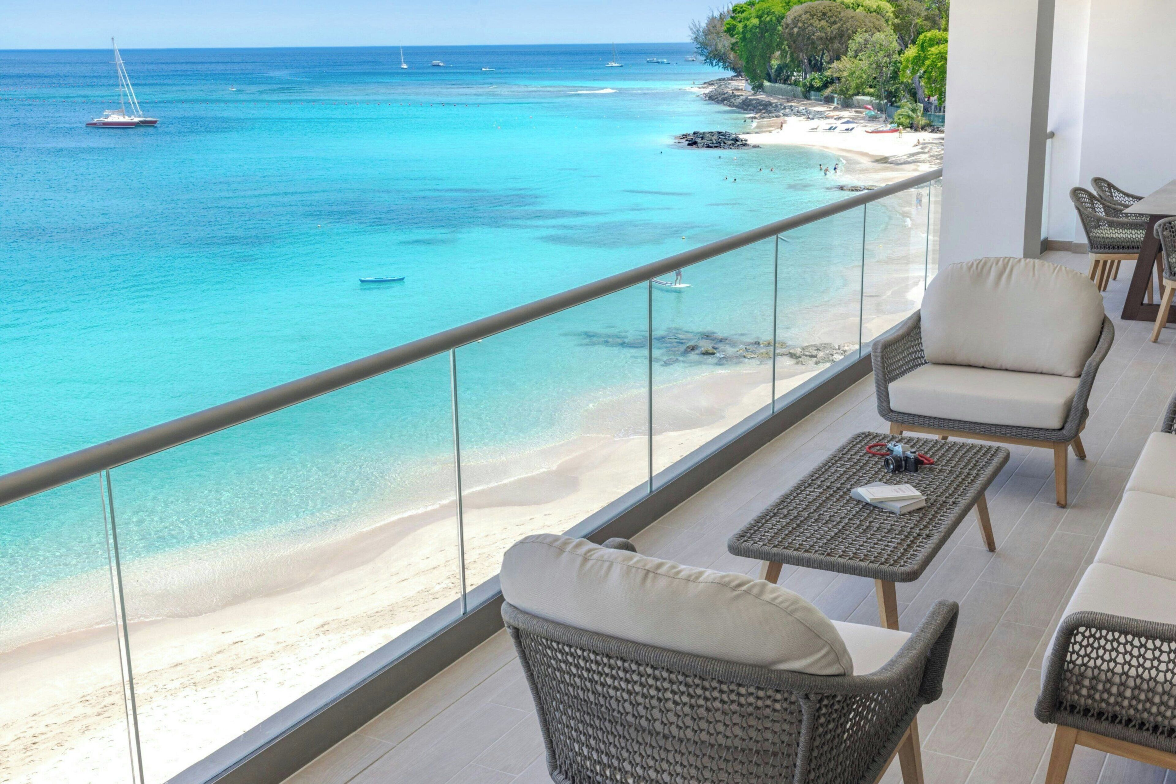 A balcony with a view of a beach and ocean, furnished with wicker chairs and a small table.