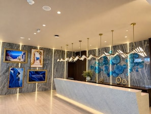 Een moderne receptiebalie met een marmeren wand, ingelijste kunstwerken, een welkomstbord en een unieke blauwe glaskunstinstallatie.