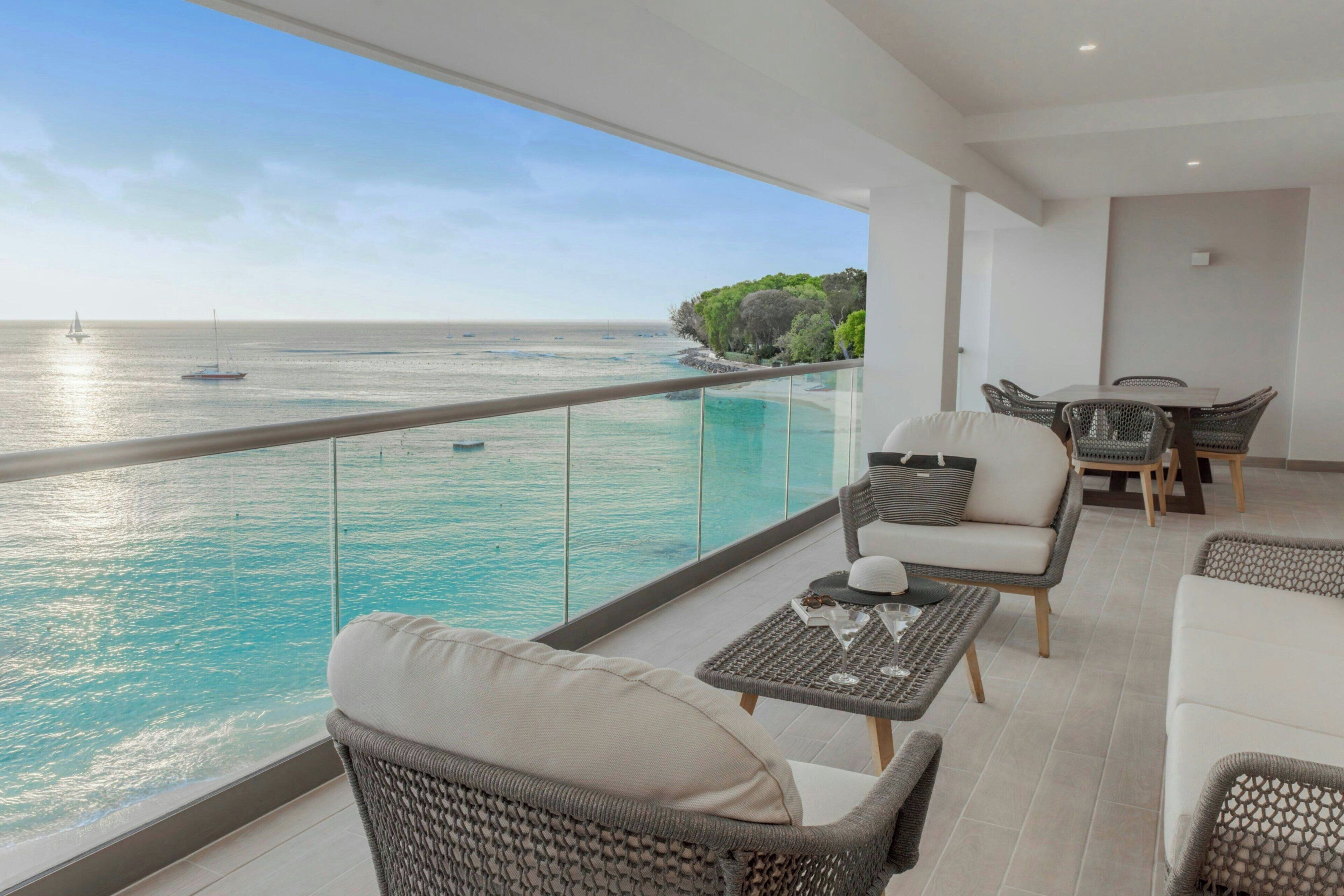 A balcony with a view of the sea, wicker furniture, and a glass railing.