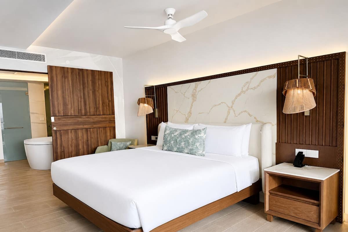 A modern bedroom with a large bed, wooden headboard, bedside tables, a ceiling fan, and a marble-patterned wall.