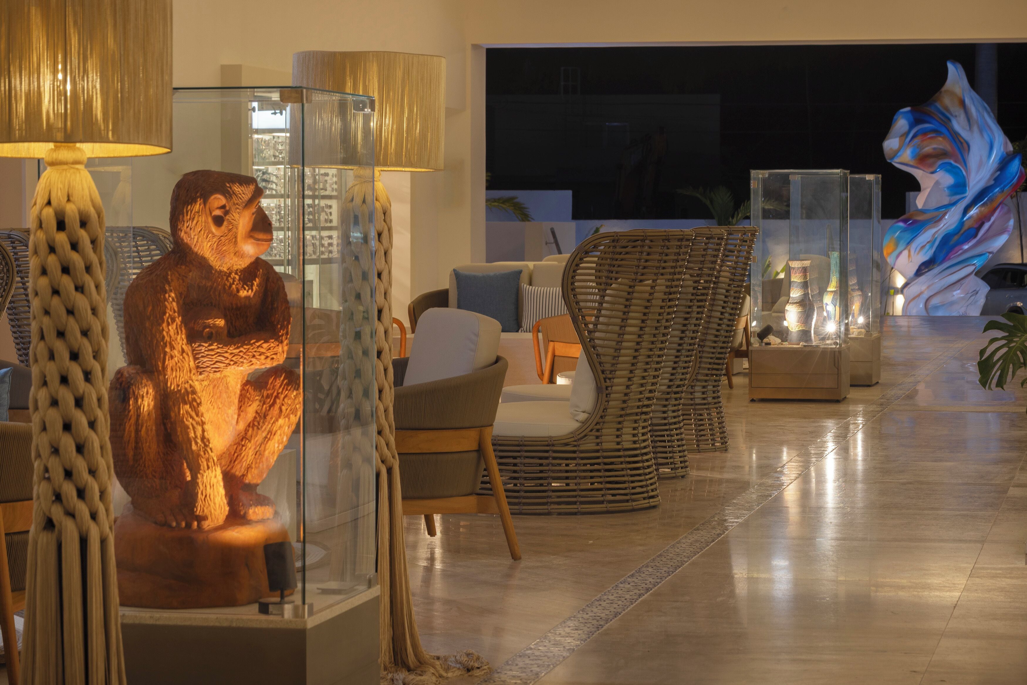 Un espace intérieur bien éclairé, avec des meubles en osier, une sculpture en verre et une lampe.