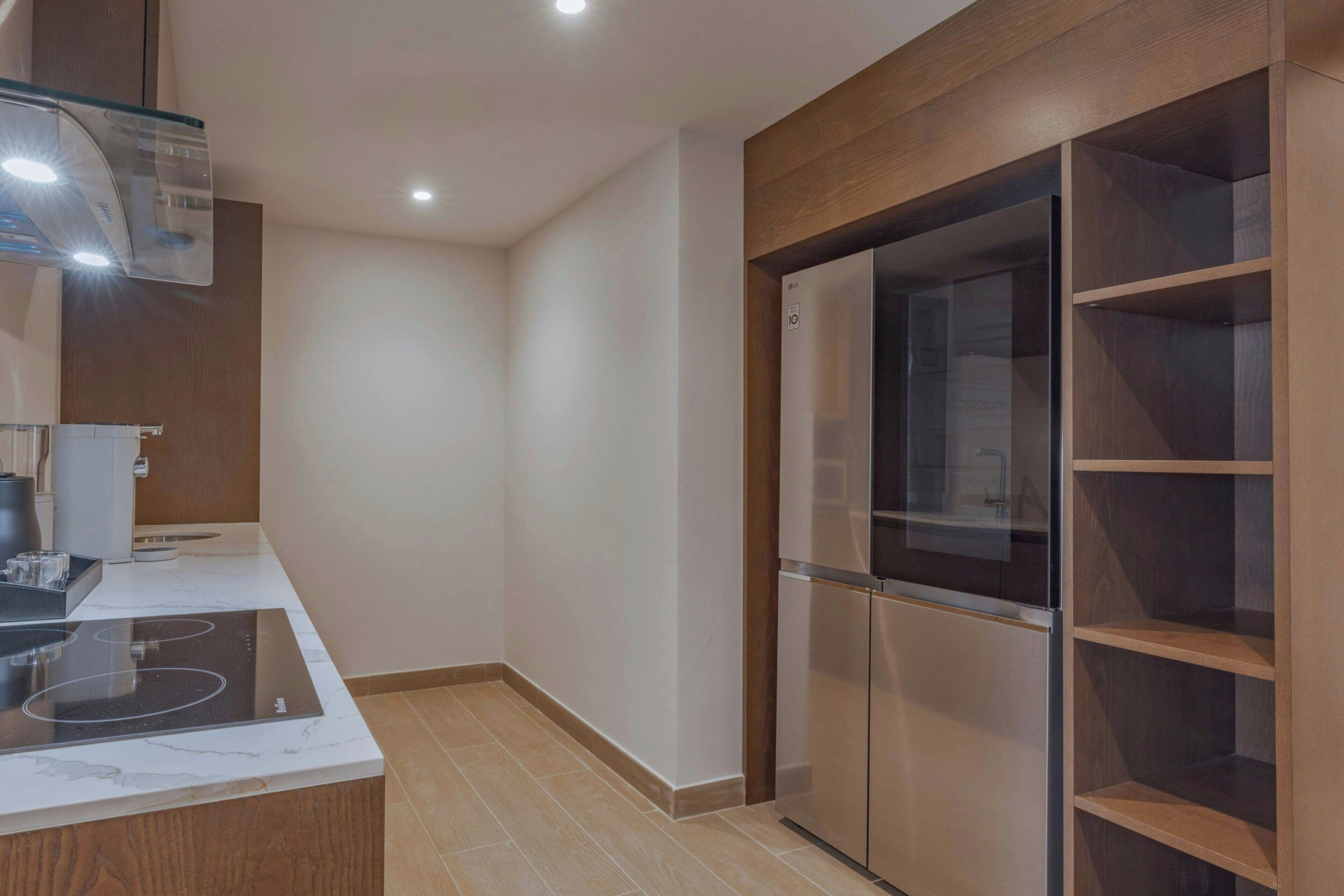 A modern kitchen with a built-in stove, a glass-fronted refrigerator, and wooden cabinetry.