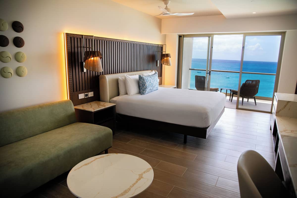 A hotel room with a bed, a sofa, a round table, and a view of the ocean.