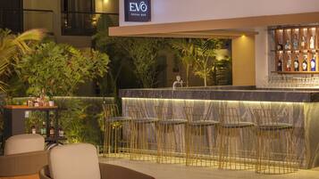 Zona de bar con un cartel que dice 'EVO SOCIAL BAR', taburetes, una barra y un área de estar con sillas.