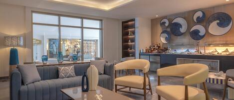 A modern living room with a sofa, chairs, a coffee table, and a kitchen area with a large window and decorative wall art.