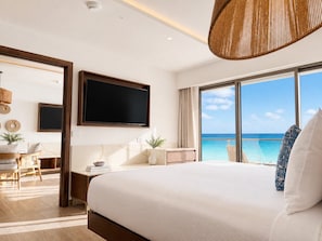 A modern hotel room with a large bed, a flat-screen TV, a desk, and a view of the ocean.