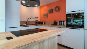 A modern kitchen with white cabinets, a black induction cooktop, a microwave, and an oven. - Maison Kerzuc - Entre mer et forêt (Crac'h)