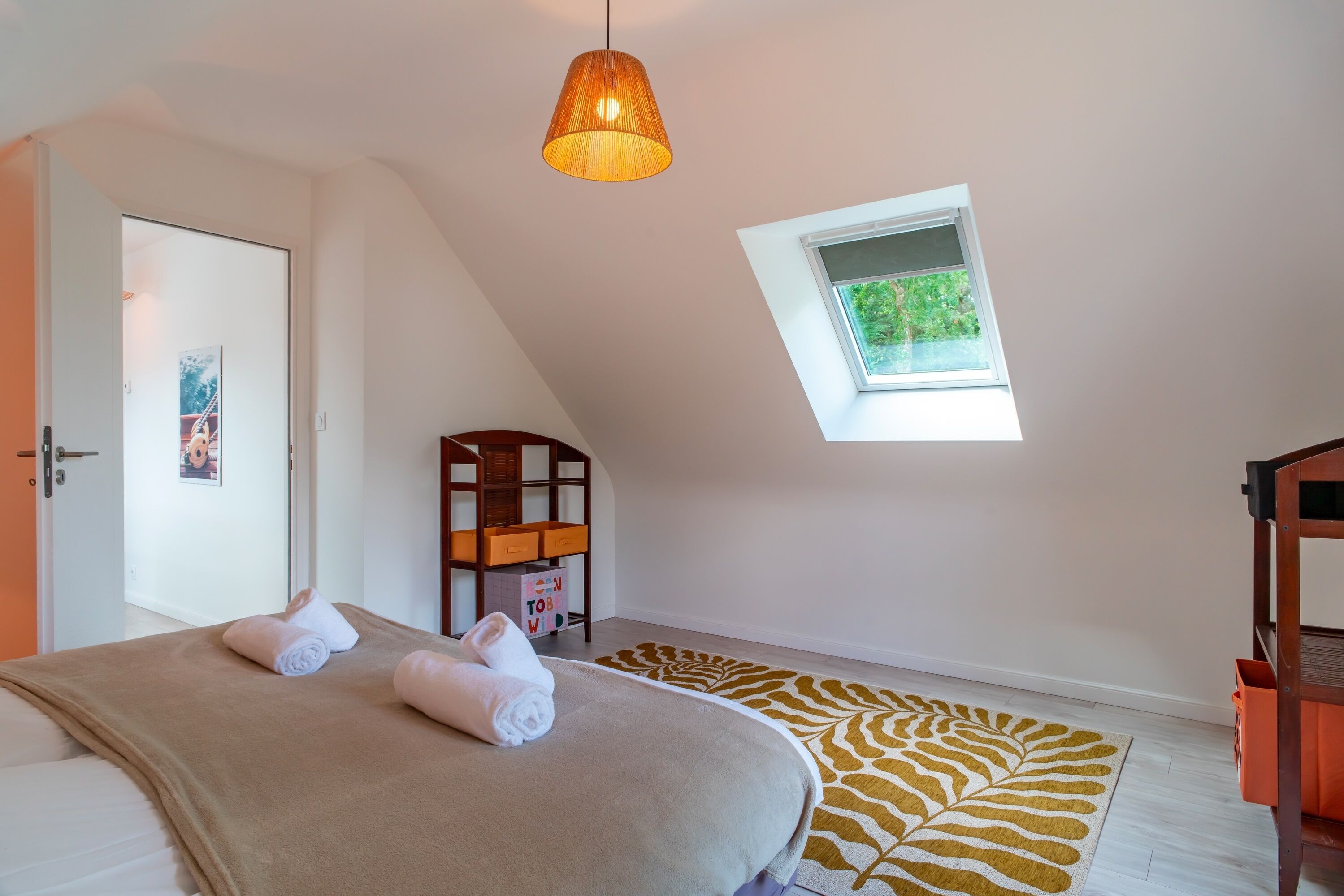 A bedroom with a bed, a window, a ceiling lamp, and a small wooden shelf.