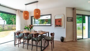 A dining area with a wooden table and chairs, a hanging light fixture, and a view of the outdoors. - Maison Kerzuc - Entre mer et forêt (Crac'h)