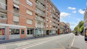 Un immeuble à plusieurs étages, doté d’une rangée de balcons, d’un arrêt de bus et surplombant un ciel dégagé.