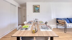 Ein Essbereich mit einem Holztisch, gedeckt für vier Personen, Stühlen, einem Bild an der Wand und einem Bett mit Metallgestell im Hintergrund.