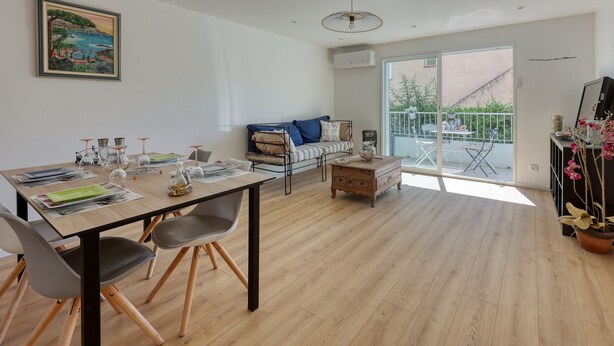 Ein modernes Wohnzimmer mit Essbereich, einer Couch, einem Couchtisch und einem Balkon mit Gartenmöbeln.