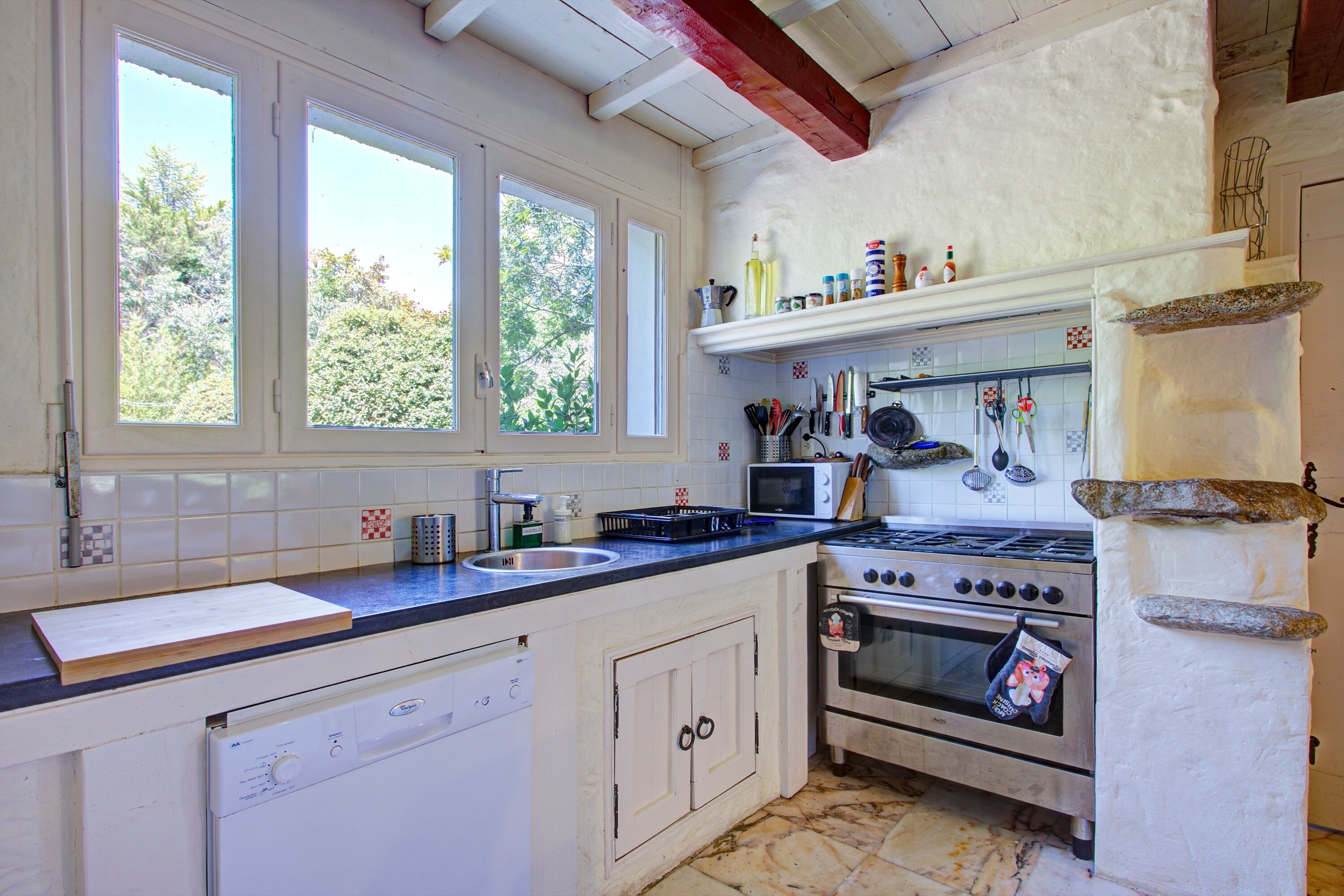 A kitchen with a stove, oven, microwave, and sink. There are cabinets, a window, and a shelf with kitchen items.