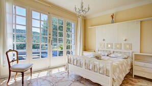 A bedroom with a large window, a bed, a chair, and a wardrobe. - Catlove - Piscine Privée (Eus)